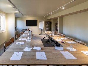 Ein Konferenzraum mit langem Tisch, Stühlen, einer Projektionsleinwand und einer Whiteboard-Tafel.