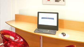 Un espace d’accueil avec un bureau en bois, un ordinateur portable, deux chaises rouges et une affiche au mur.