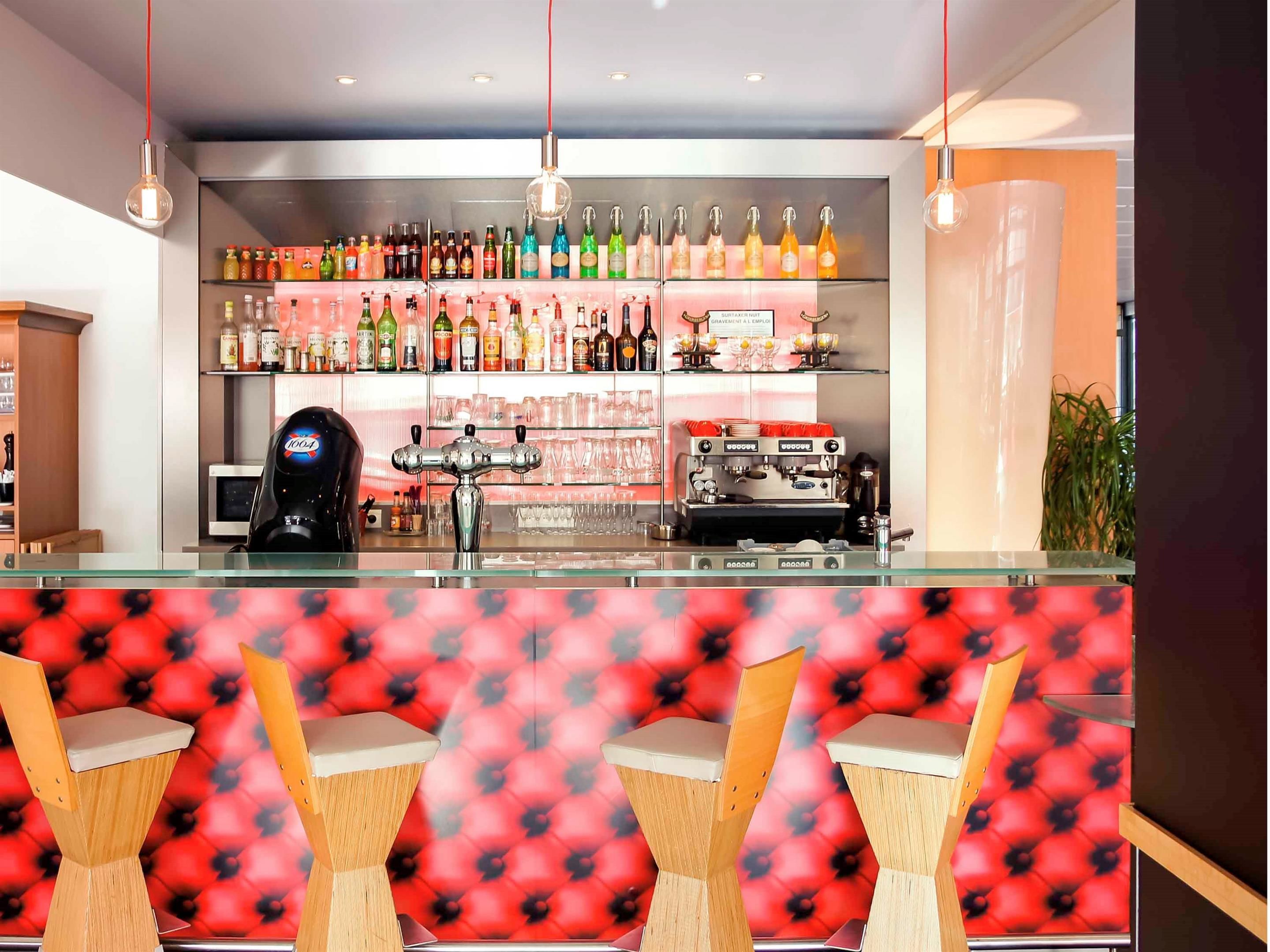Un espace bar avec un assortiment de bouteilles et un appareil à café. Des fauteuils confortables sont disposés devant le bar.