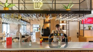 A bar area with a bartender, a neon beer mug sign, hanging glass lights, and a menu board. - ibis Metz Centre Cathédrale (Metz)