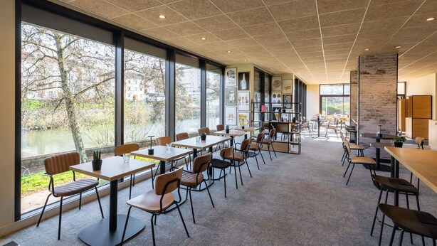 A spacious indoor area with large windows, tables, chairs, and a view of a river. - ibis Metz Centre Cathédrale (Metz)