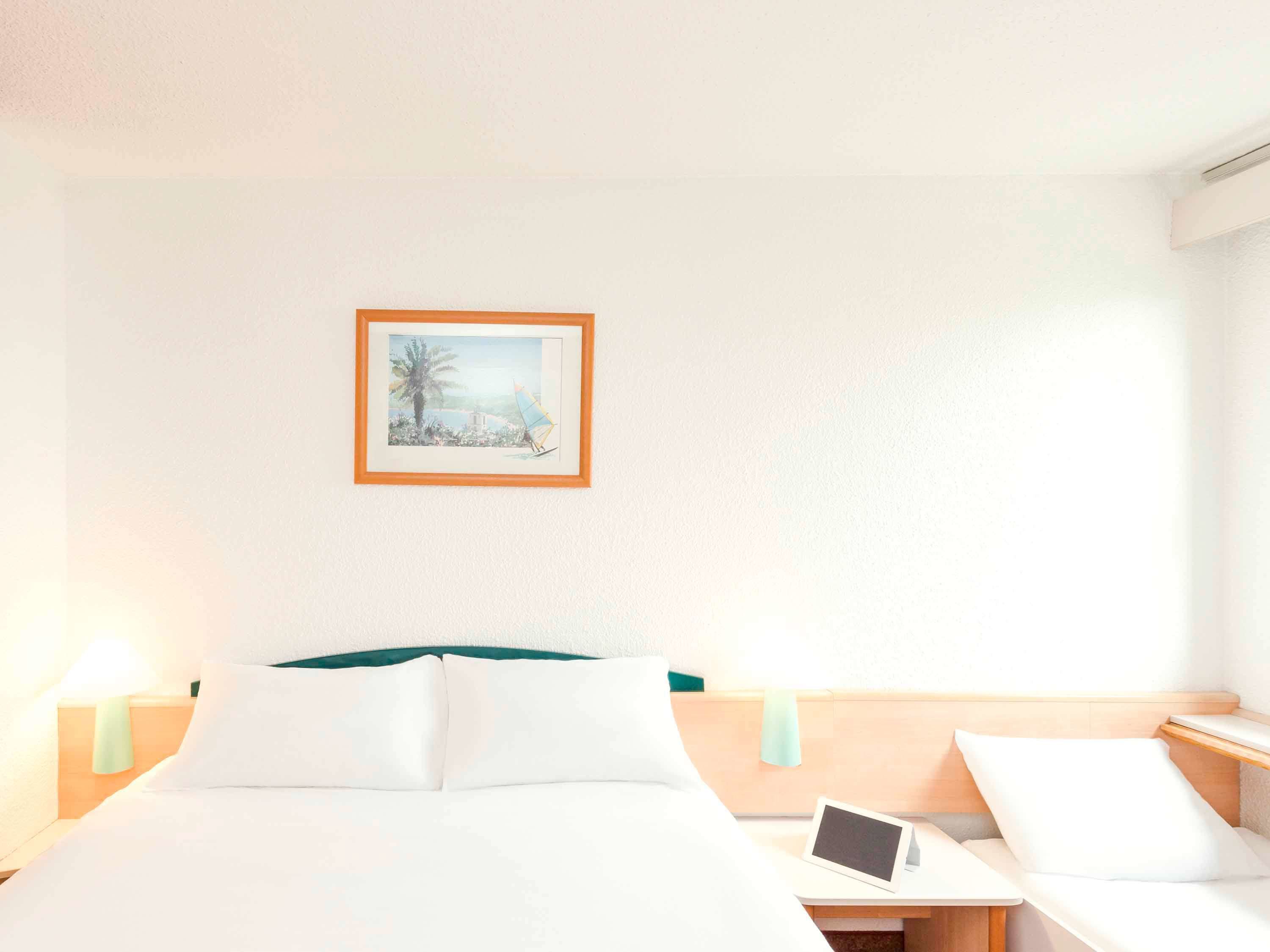 A hotel room with a bed, bedside tables, a tablet on one table, and a framed picture on the wall.