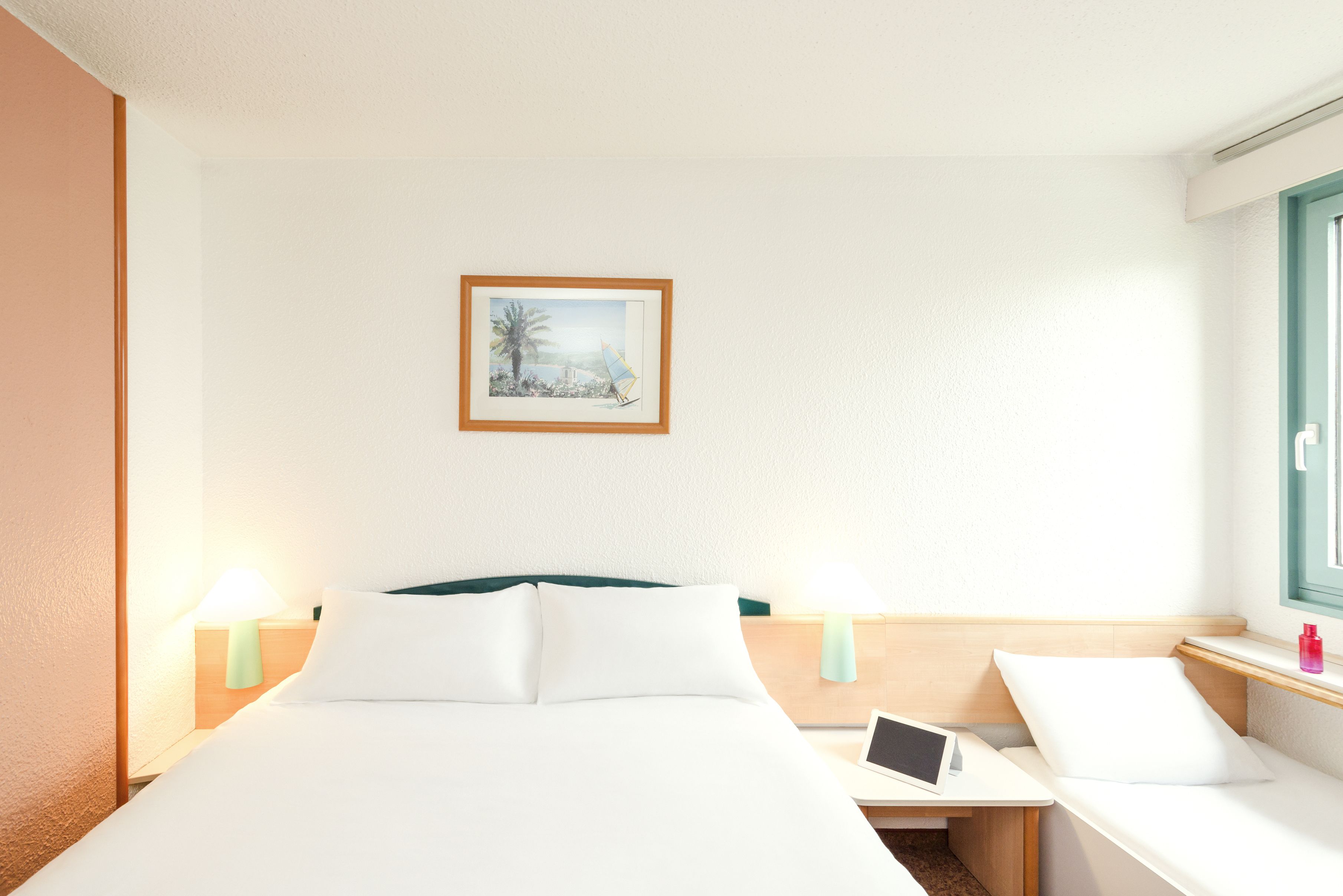 A hotel room with a bed, bedside tables, a desk with a laptop, and a framed picture on the wall.
