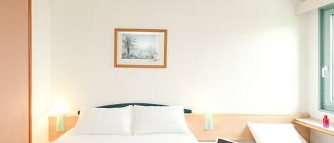 A hotel room with a bed, bedside tables, a desk with a laptop, and a framed picture on the wall.