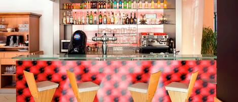 A bar area with a counter, multiple shelves of bottles, a coffee machine, and three wooden chairs with cushioned seats.