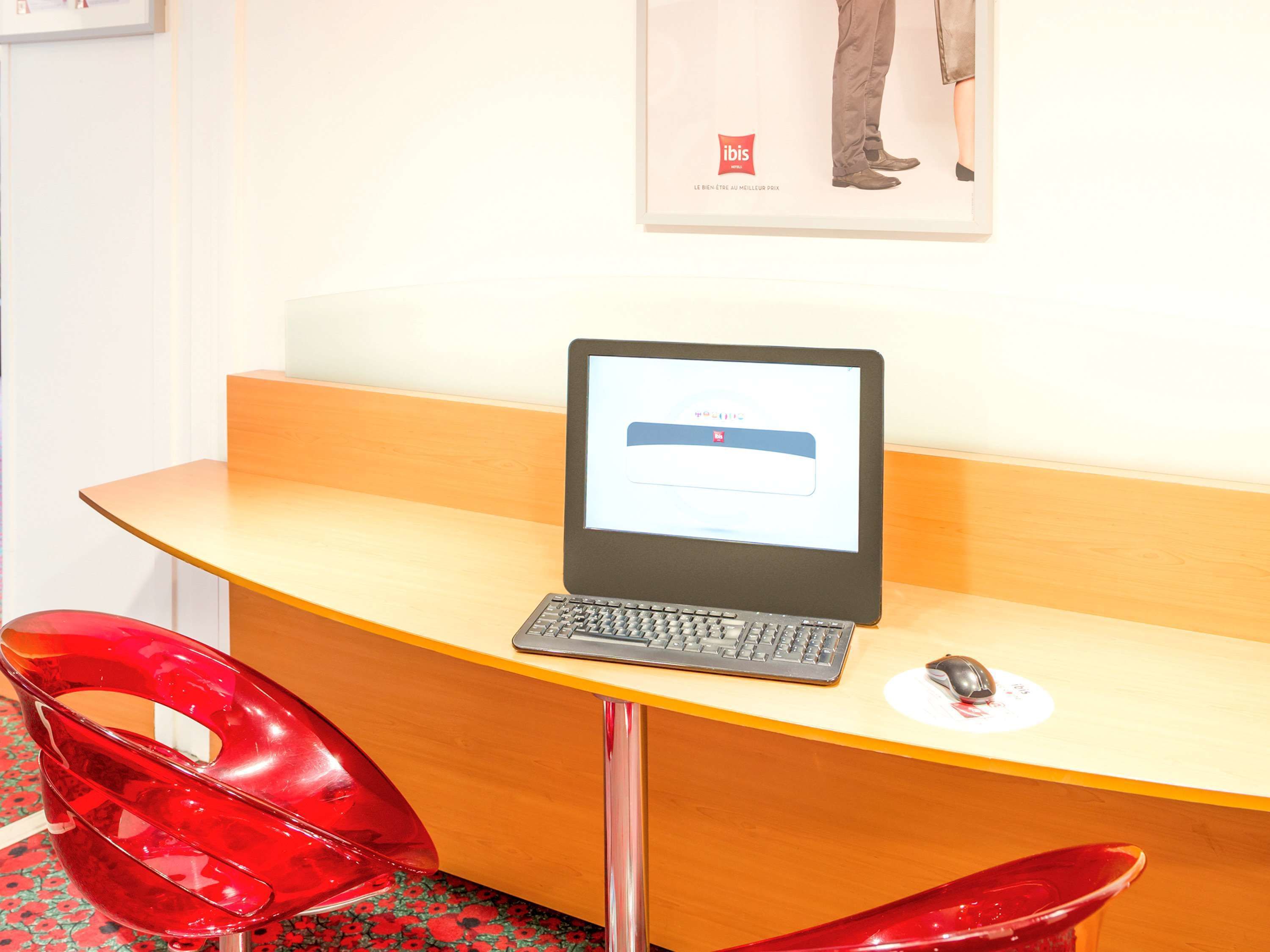 A wooden desk with a laptop and a mouse, a red chair, and a poster on the wall.