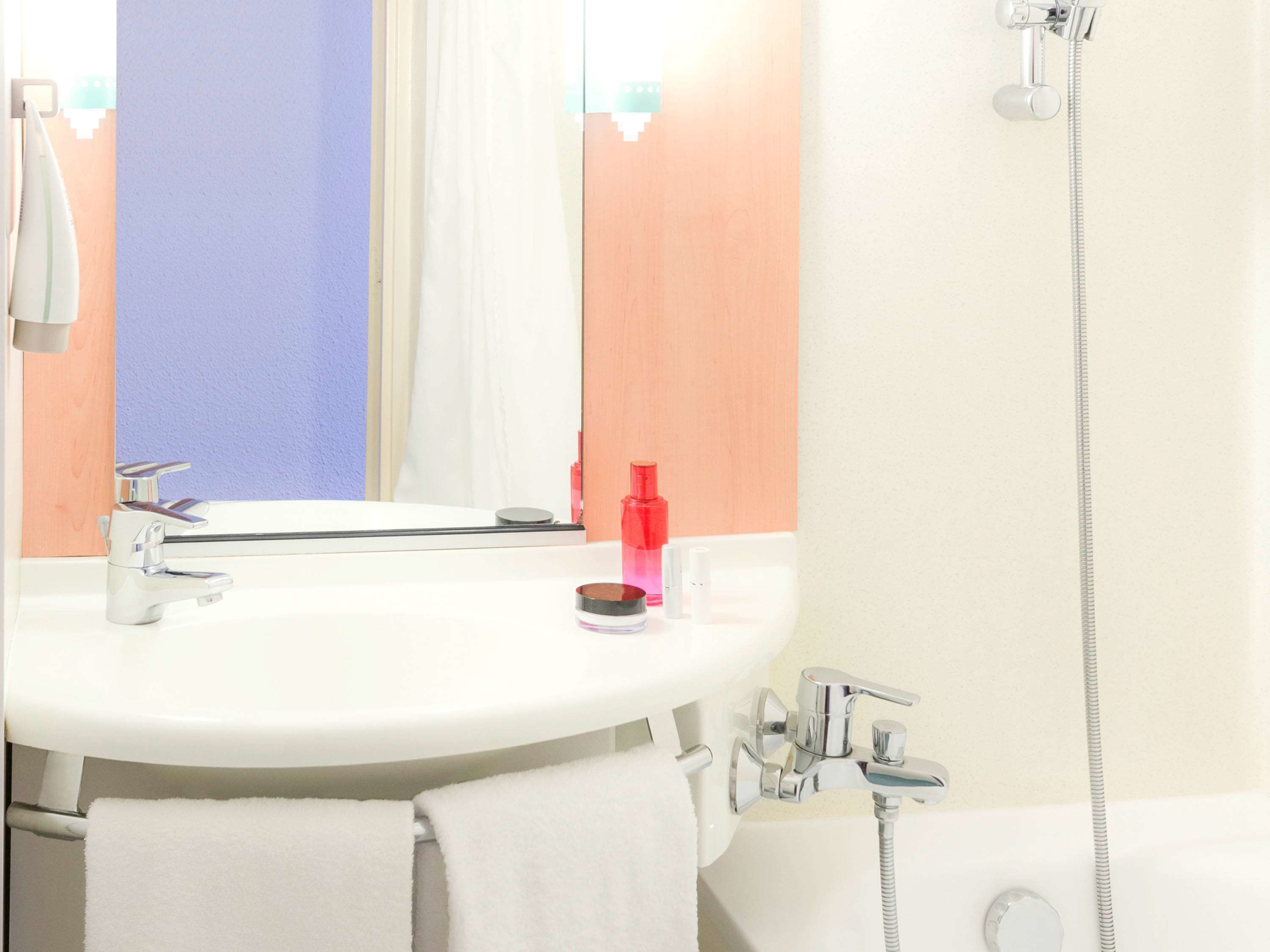 A bathroom with a white sink, a mirror, a shower, and a towel rack.