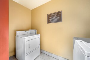 Un cuarto de lavandería con lavadora y secadora Whirlpool, un letrero que indica uso para huéspedes, y una pared amarilla.