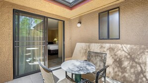Een zonnig balkon met een schuifdeur, een klein rond tafeltje en een stoel.