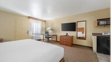 A hotel room with a bed, desk, chair, dresser, TV, and a kitchenette.