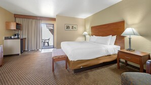 Een hotelkamer met een bed, nachtkastjes, een bureau, een stoel, een kleintje en een kitchenette.