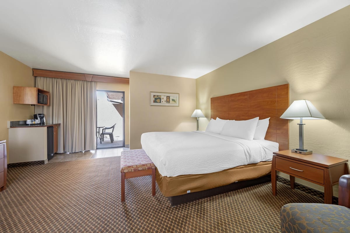 A hotel room with a bed, bedside tables, a desk, a chair, a small table, and a kitchenette.