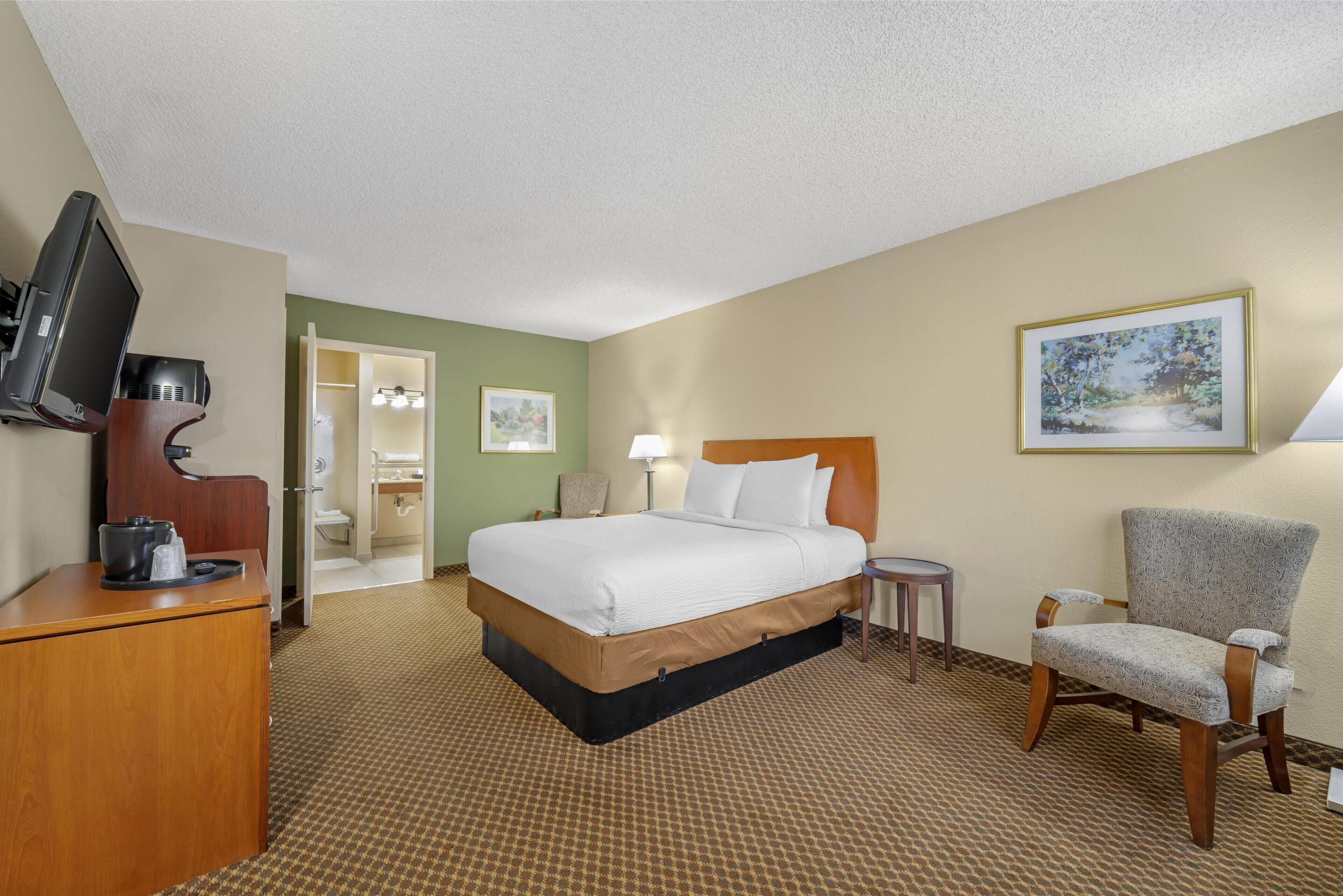 Habitación de hotel con cama, escritorio con televisor, una silla y baño visible a través de una puerta abierta.