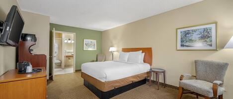Habitación de hotel con cama, escritorio con televisor, una silla y baño visible a través de una puerta abierta.