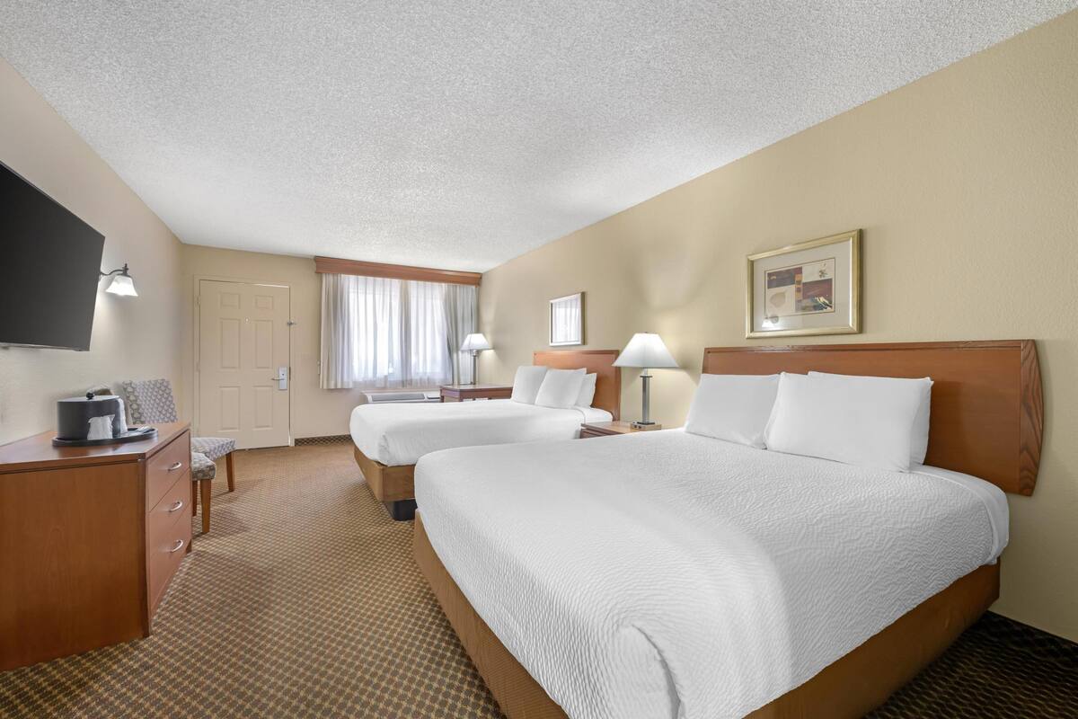 A hotel room with two beds, a desk, a TV, and a window with curtains.