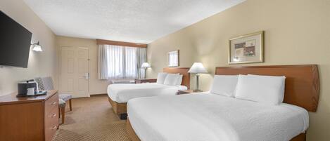 A hotel room with two beds, a desk, a TV, and a window with curtains.