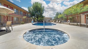 Een zwembad met een jacuzzi, ligbedden en een heldere lucht.