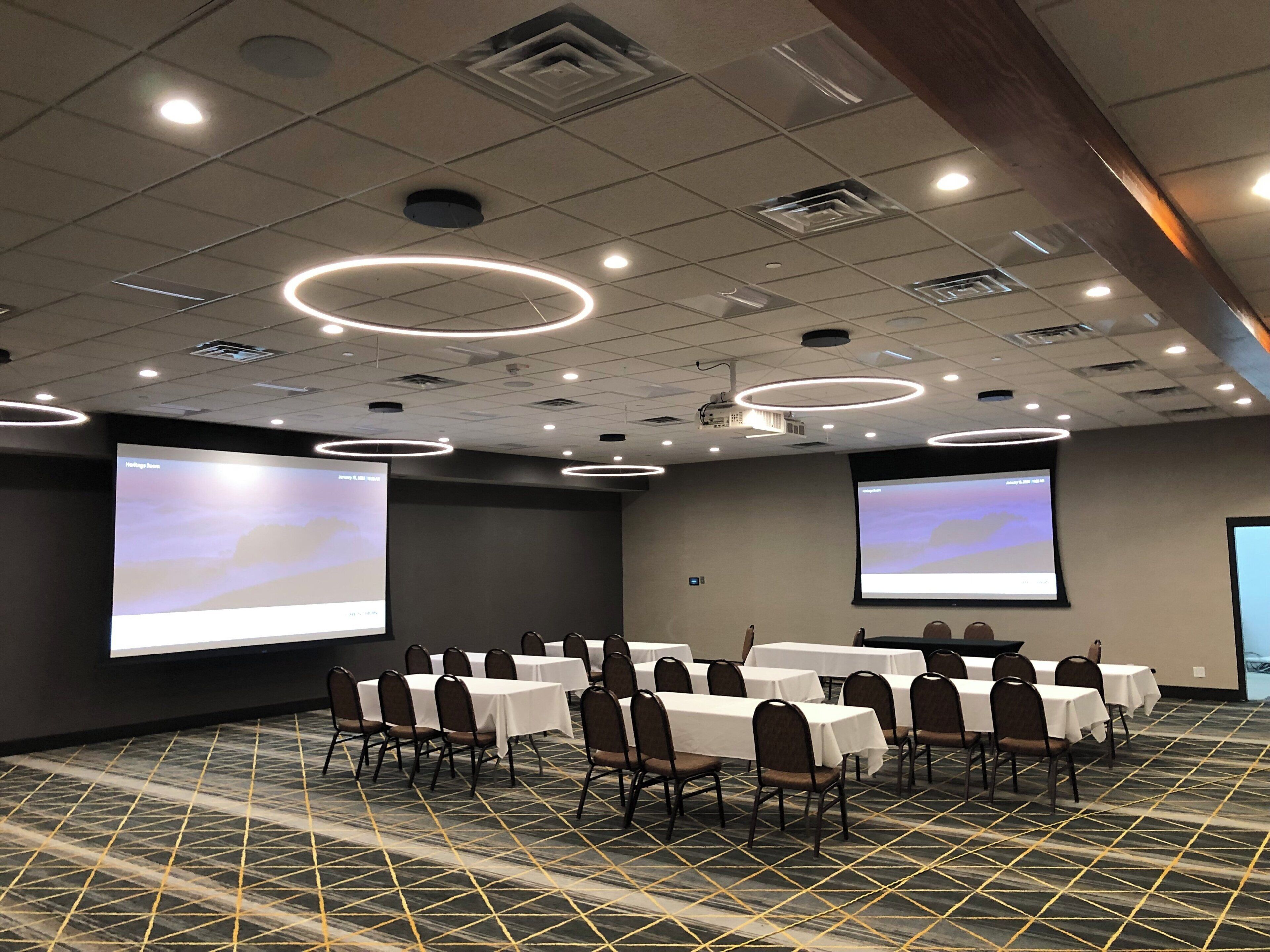 Un salón de conferencias con varias mesas y sillas, pantallas grandes y un diseño de techo moderno.