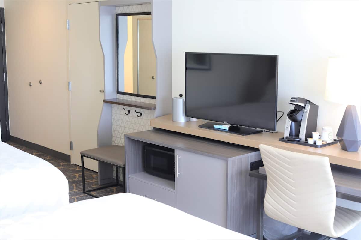 A hotel room with a bed, a desk with a computer, a chair, a microwave, and a coffee maker.