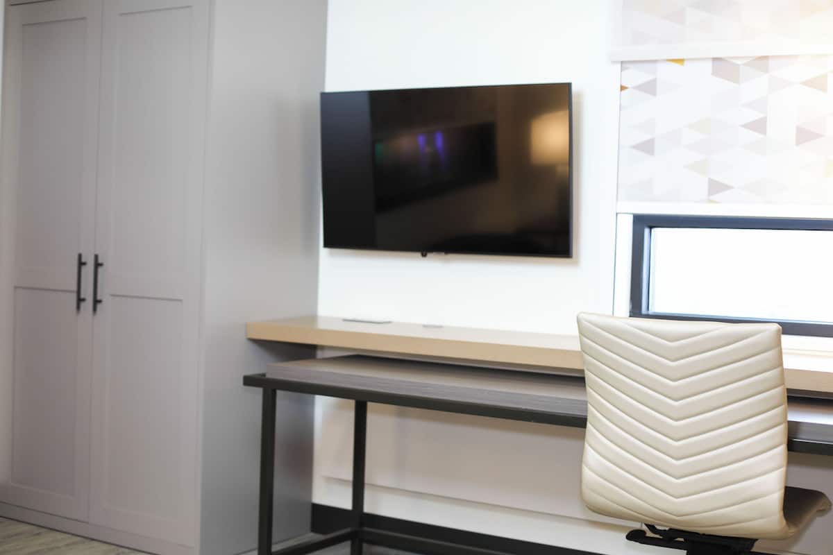 A modern room with a TV mounted on the wall, a desk with a chair, and a wardrobe.