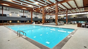 An indoor swimming pool with a tiled floor, wooden beams, and a staircase leading to upper levels.