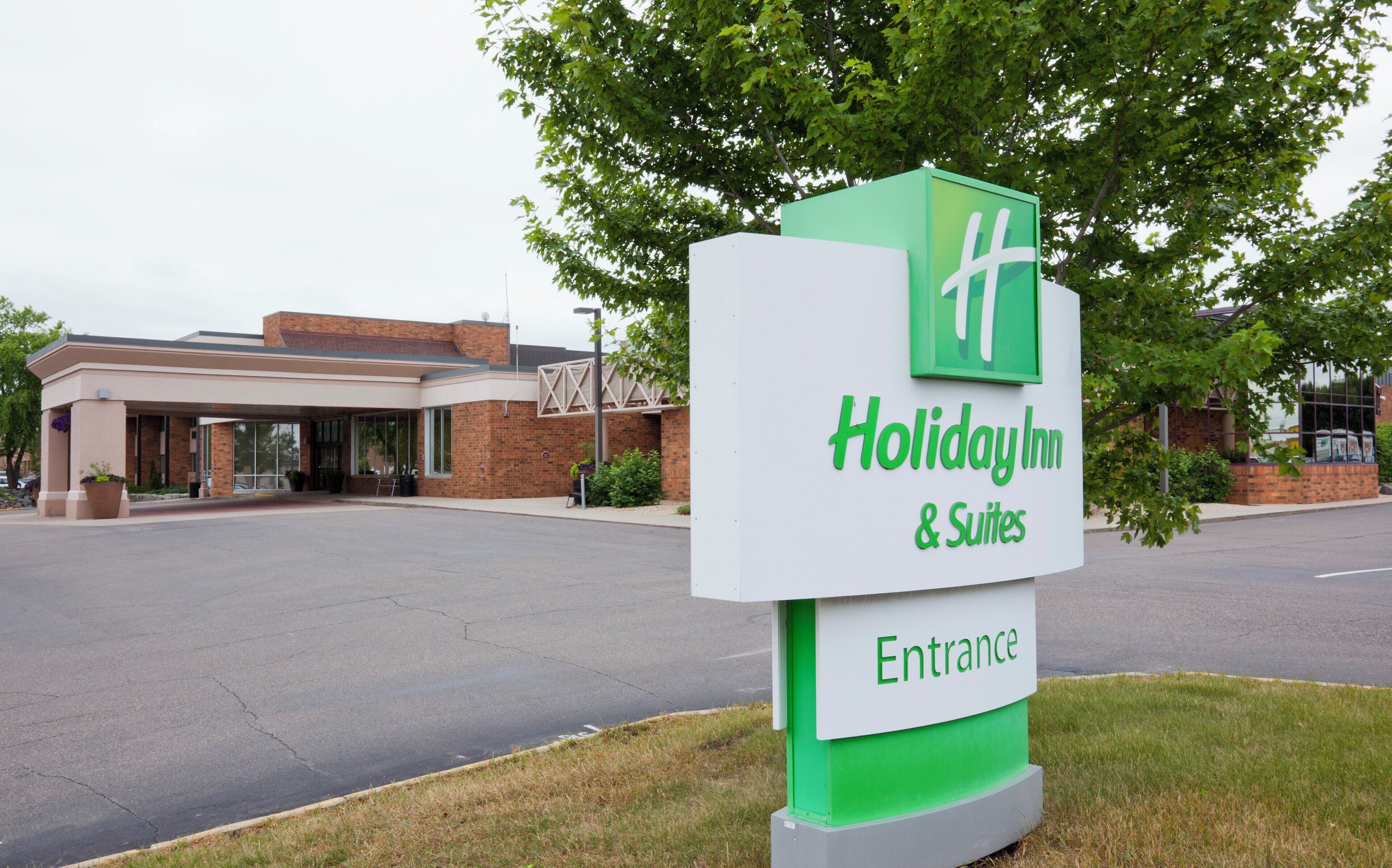 A Holiday Inn & Suites sign with a green and white color scheme, indicating the entrance to the hotel.