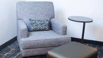 A grey armchair with a patterned pillow, a small round table, and a matching ottoman.