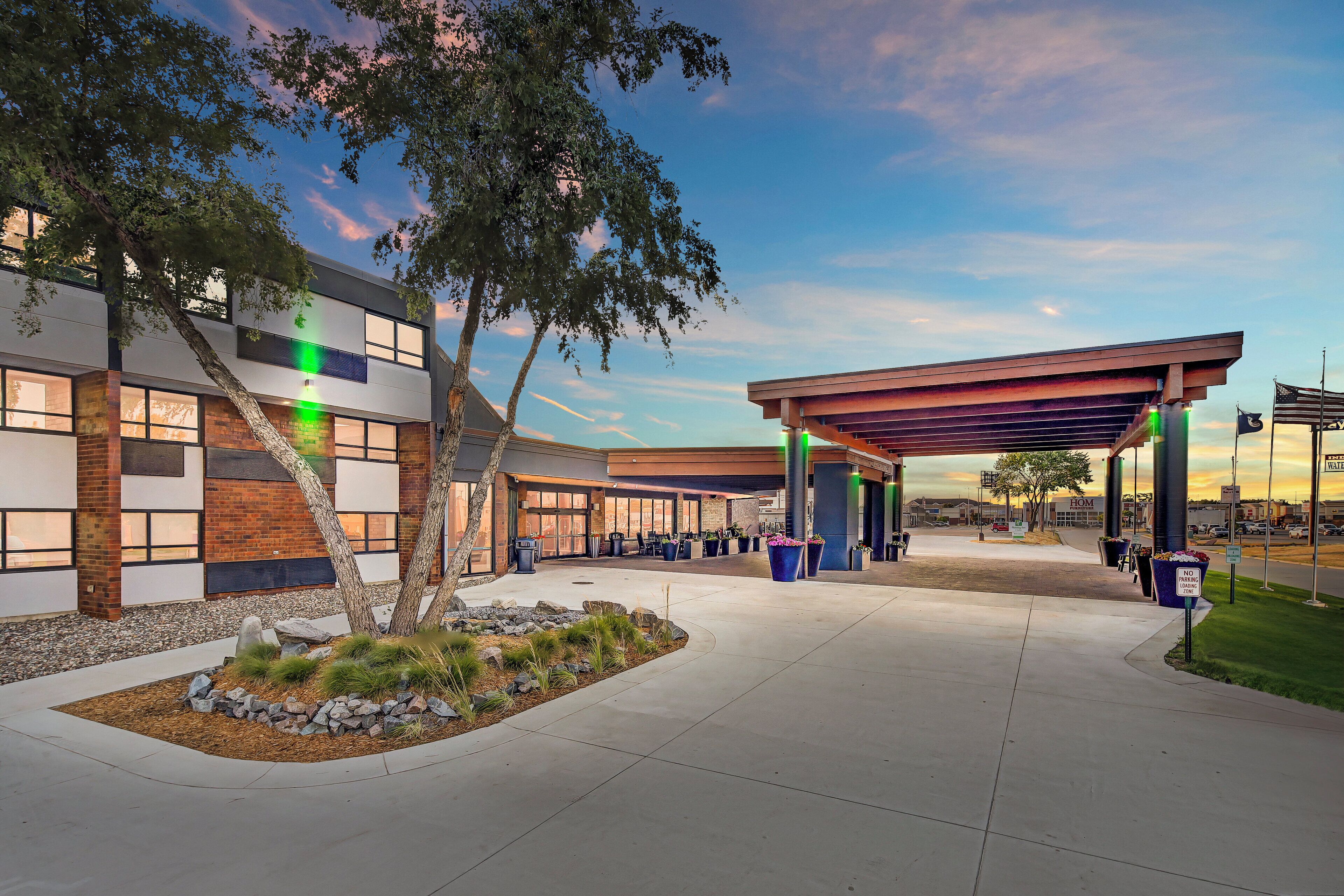 A modern building with a covered entrance, outdoor seating area, and a landscaped garden.