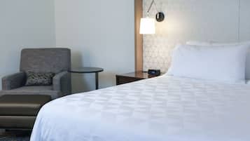 Una habitación de hotel con cama, una silla, una mesita y una mesita de noche.