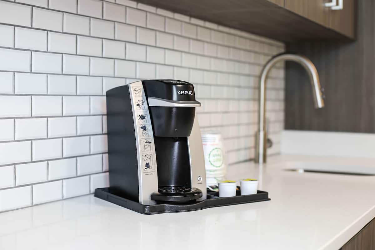 A modern coffee maker on a kitchen counter with a white tiled backsplash and a stainless steel faucet.