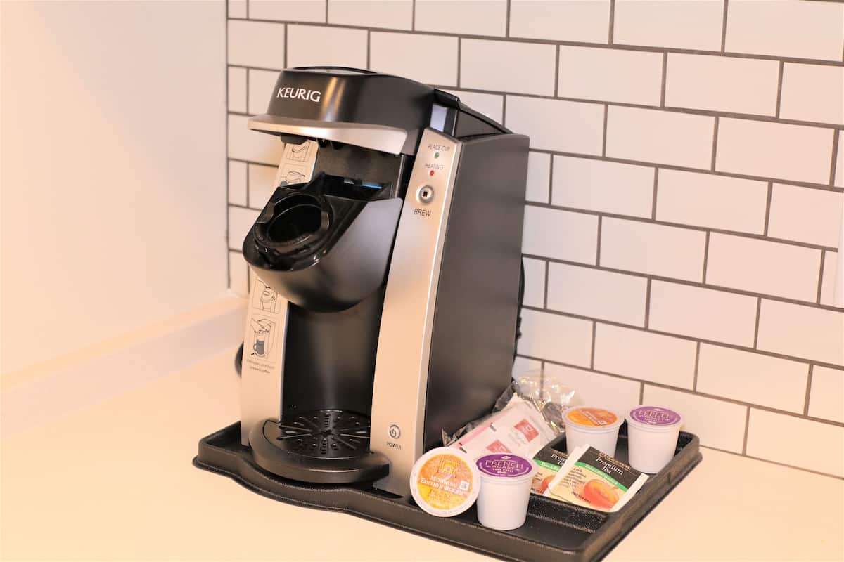 A Keurig coffee machine with a drip tray containing a French press and two disposable cups.