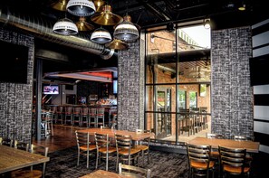 An indoor dining area with multiple tables and chairs, a bar area with a counter and stools, and large windows allowing natural light. - Holiday Inn & Suites St. Cloud by IHG (St Cloud)