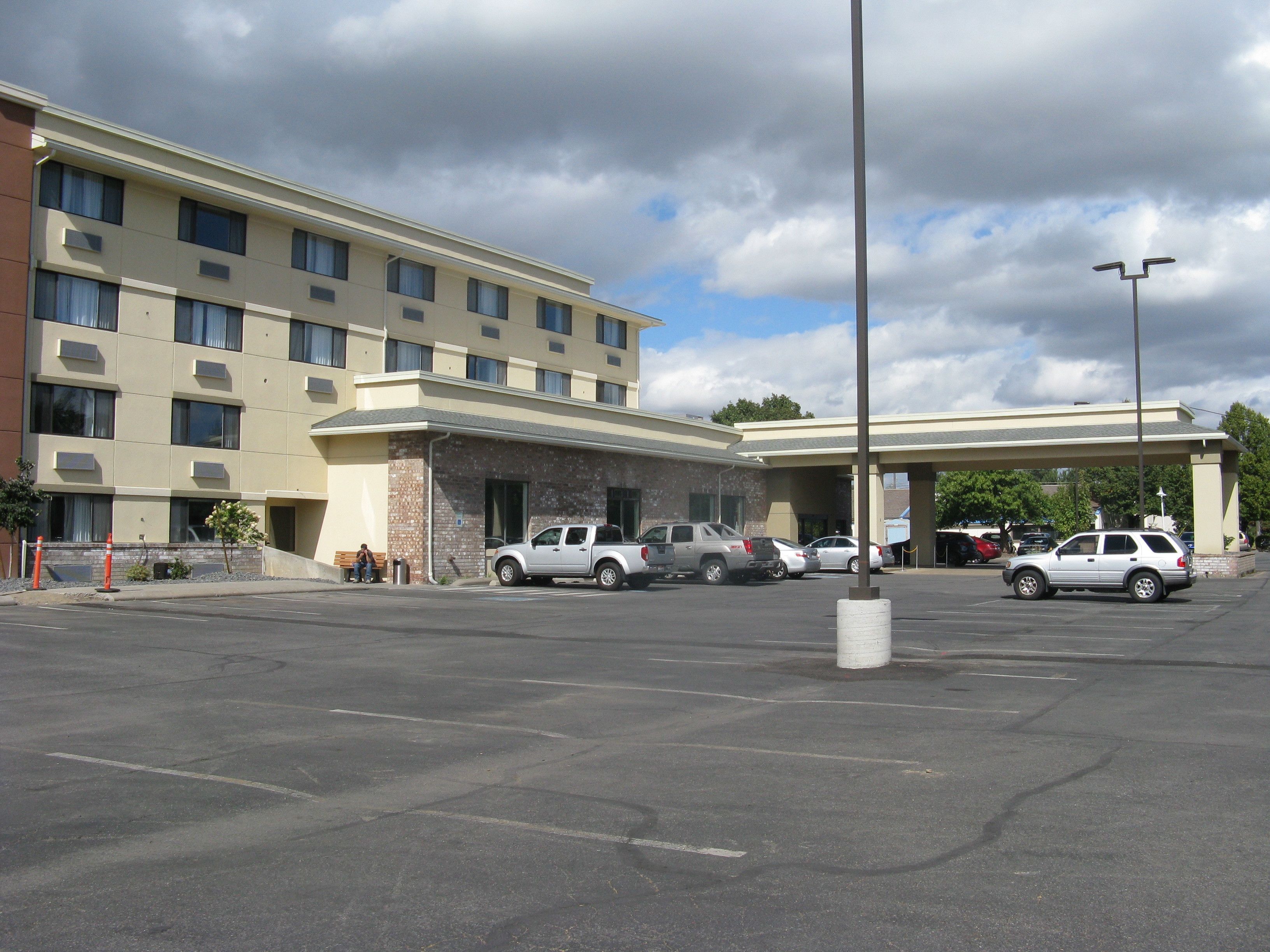 A hotel with a parking lot, multiple cars, and a covered walkway.