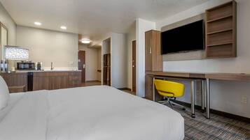 A hotel room with a bed, a desk with a chair, a television, and a kitchenette.