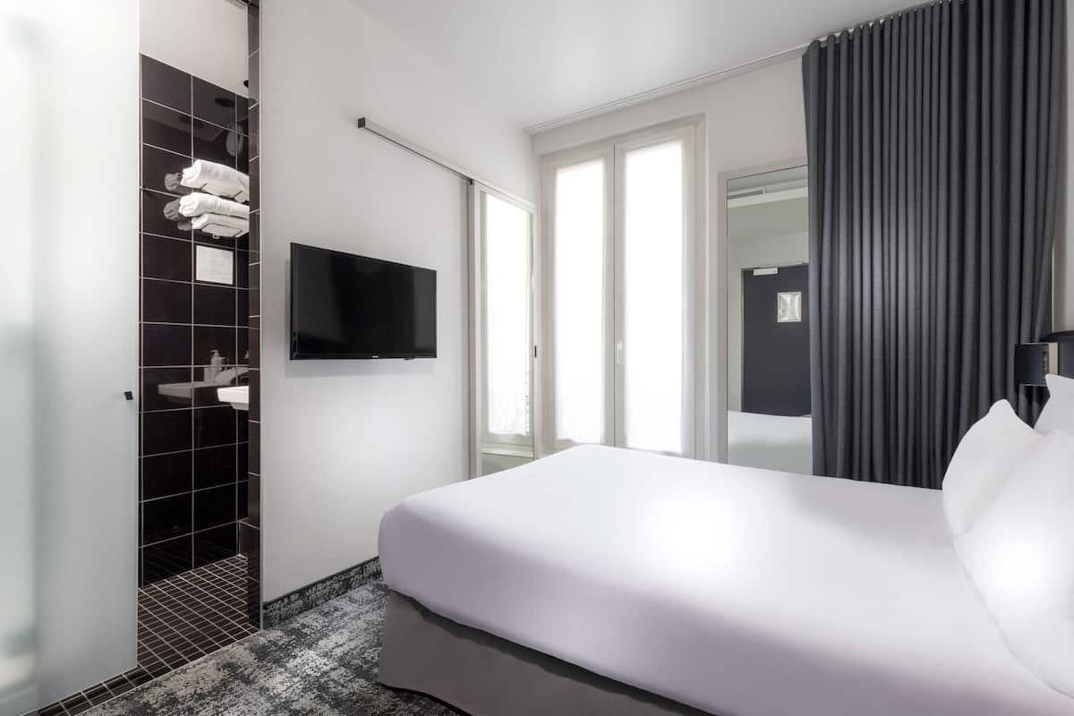 Een hotelkamer met een bed, een televisie, een douche en een raam met gordijnen.