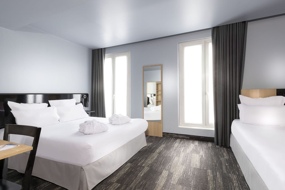 Een hotelkamer met een groot bed, een bureau, een stoel, een spiegel en twee ramen voorzien van gordijnen.