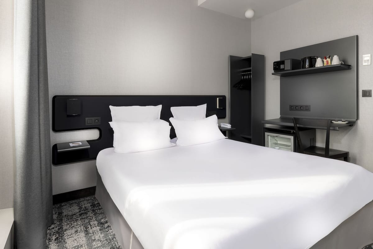 Een moderne hotelkamer met een groot bed, nachtkastjes, een ingebouwde televisie en een minibar.