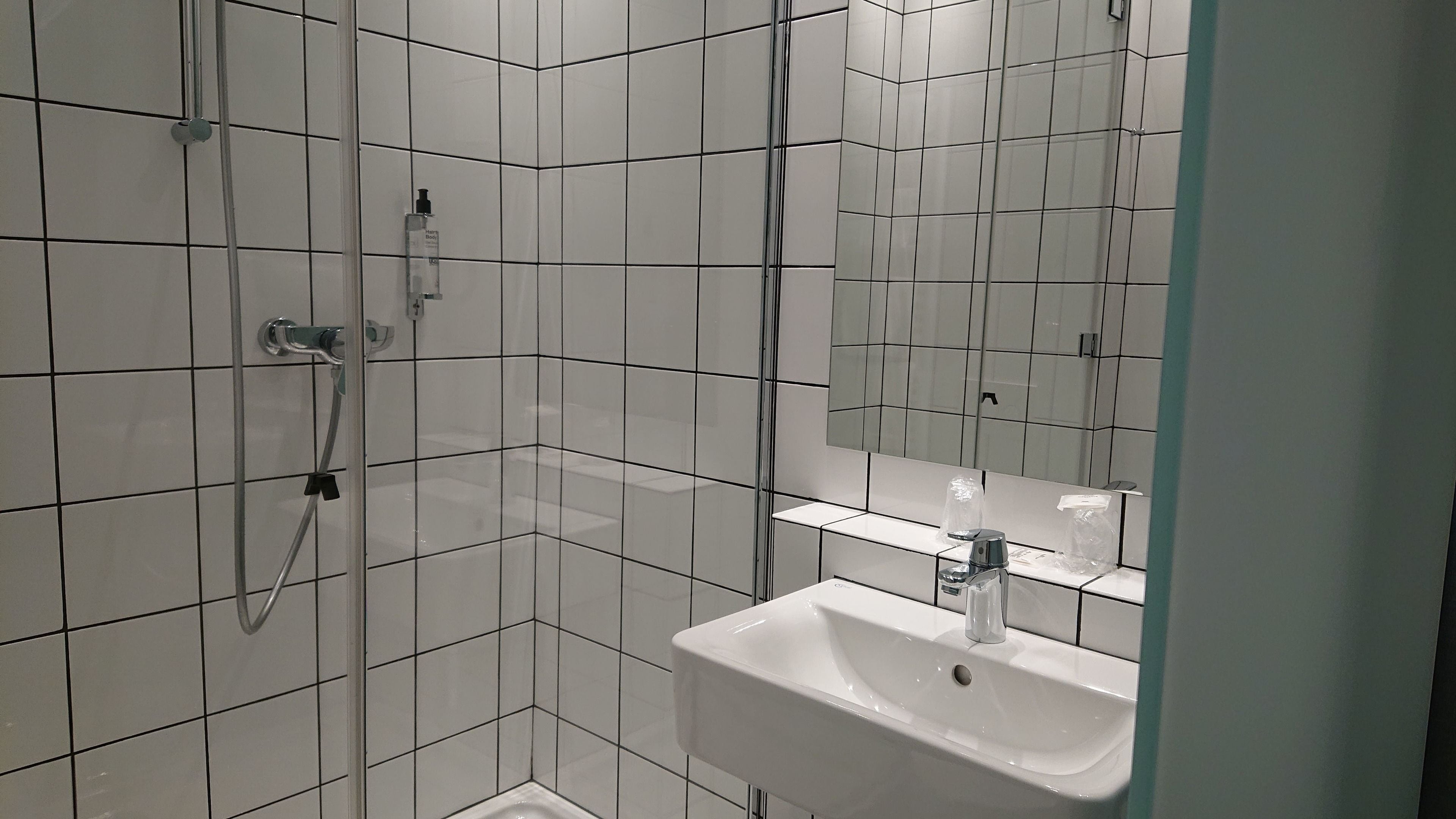 A modern bathroom with white tiles, a glass shower enclosure, a sink with a mirror, and a handheld showerhead.