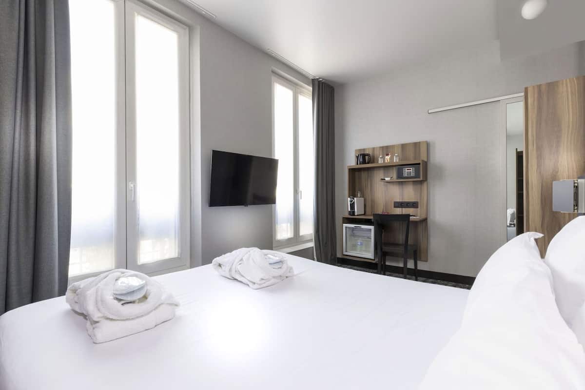 Een moderne hotelkamer met een groot bed, twee handdoeken, een televisie, een minibar en een wandpaneel van hout.