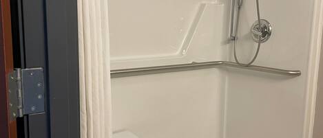 A bathroom with a shower, a white door, and a metal grab bar.