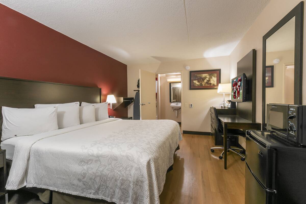 A hotel room with a large bed, a desk, a TV, a microwave, and a refrigerator.