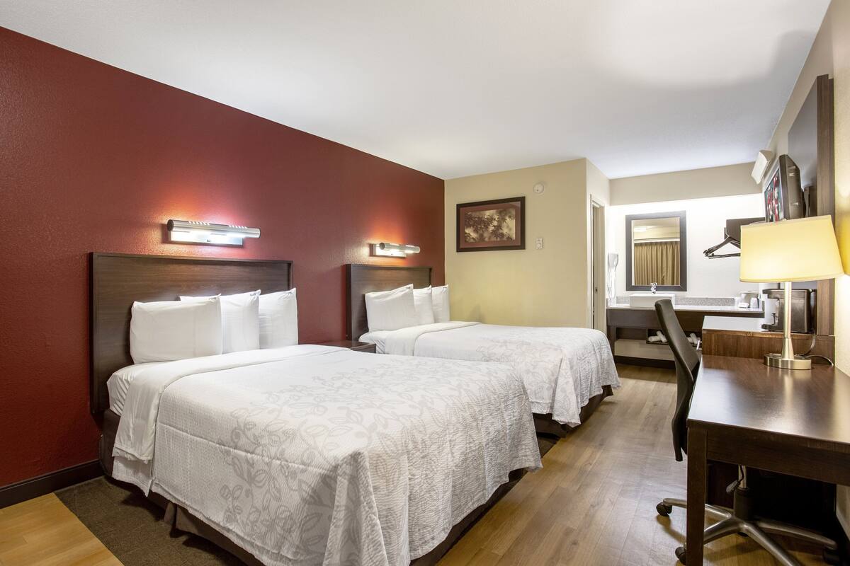 A hotel room with two beds, a desk, and a mirror.
