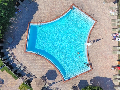 An aerial view of a swimming pool with a tiled deck surrounding it, equipped with lounge chairs and umbrellas.