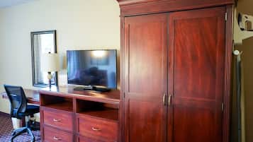 A hotel room with a wooden desk, a television, a chair, and a wardrobe.
