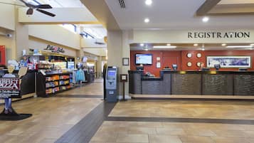 Zona de registro de hotel con mostrador de recepción, un reloj y una pantalla mostrando el menú del restaurante Boardwalk Buffet.