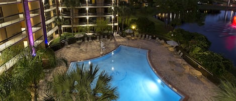 Um hotel com piscina, cercado por palmeiras e vista para um corpo d'água.