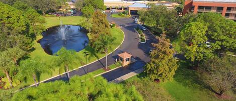 A landscaped area with a pond, a fountain, and a parking lot with vehicles.