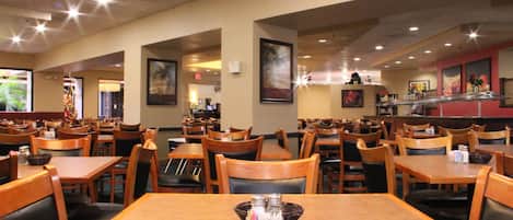A restaurant with wooden tables and chairs, framed artwork on the walls, and a counter area.