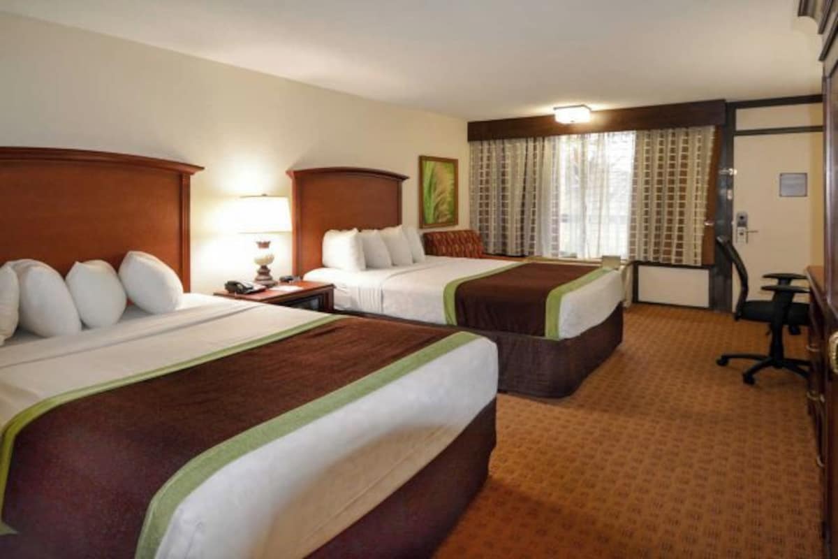 A hotel room with two beds, a desk, a chair, and a window with curtains.