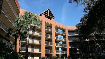 Un hôtel à plusieurs étages doté de balcons, de palmiers et surplombant un ciel d’un bleu éclatant.
